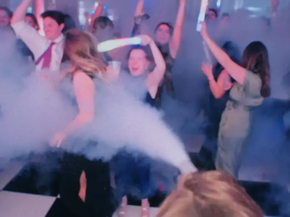 A guest fires a CO2 cannon across a packed dance floor with glow sticks in the air