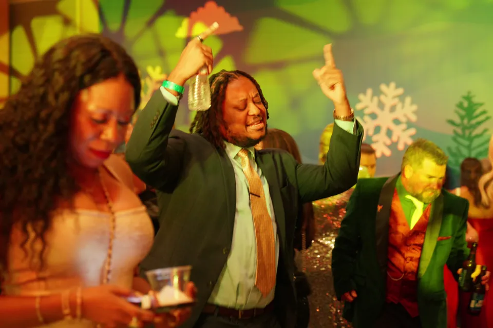 A guest in a suit and gold tie dances with one hand in the air at a company holiday party